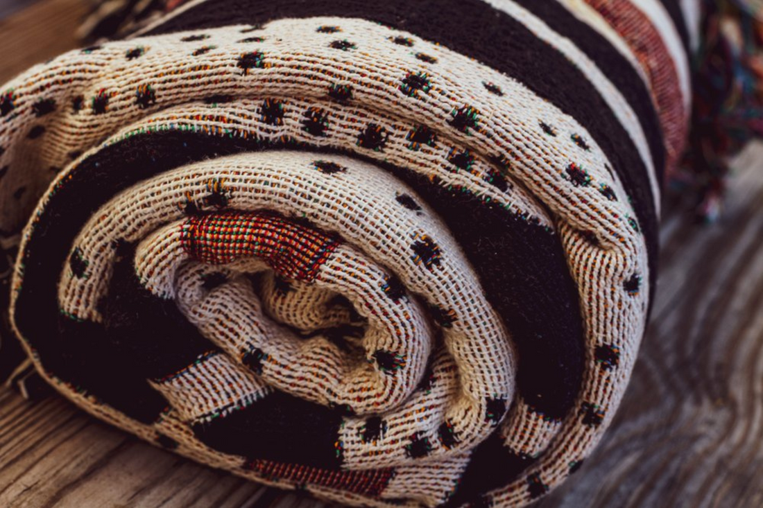 Rolled-up woven blanket with intricate patterns in earthy tones, showcasing artisanal craftsmanship and sustainable design.