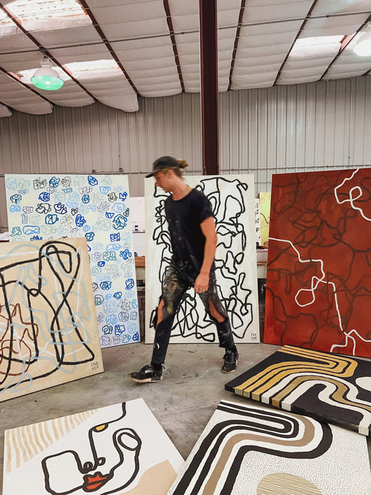 Artist walking in front of abstract painting collection in studio, moody atmosphere