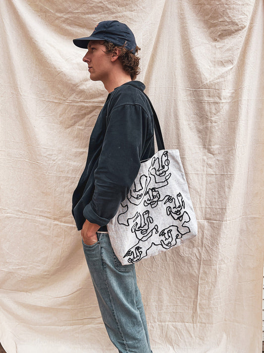 Young guy with curly blonde hair, southern california surger style, showcasing abstract art woven tote bag, fashion