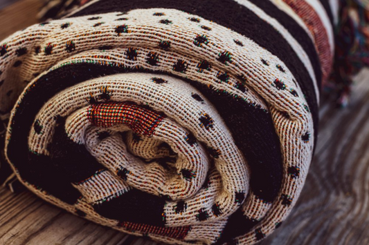 Rolled-up woven blanket with intricate patterns in earthy tones, showcasing artisanal craftsmanship and sustainable design.